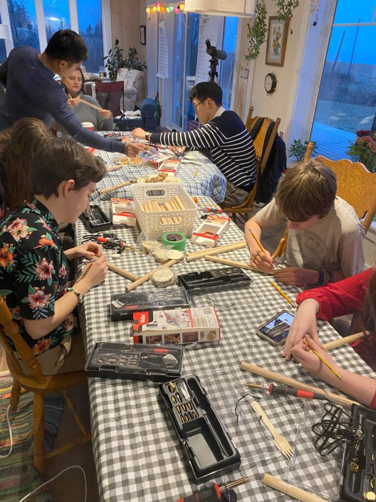 Participants use pencils to outline designs on their clapsticks, which they will later trace over with a wood-burning tool.