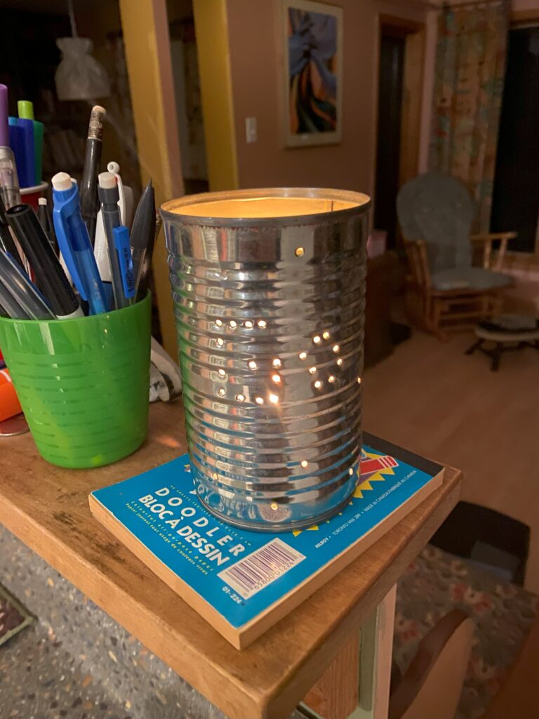 A candle burns within a tin can that had a pattern punched into it at the junior youth camp.