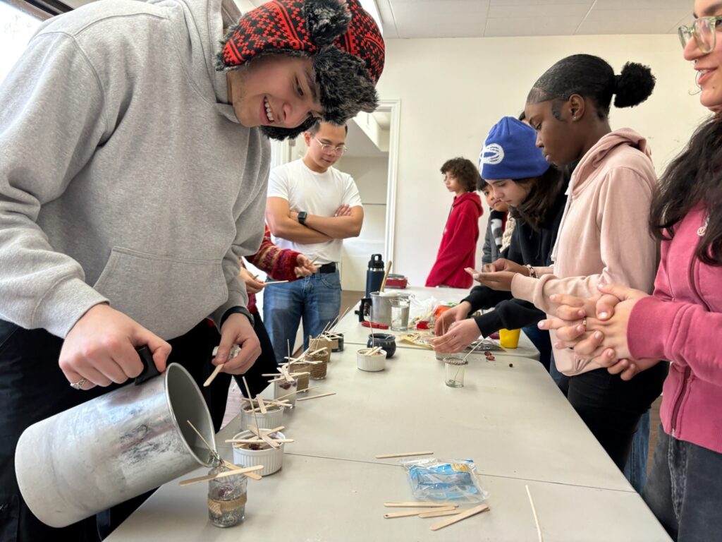 A friend visited the camp to guide the junior youth in the candle-making process. Here, he pours hot wax into the candle jars that the junior youth had decorated.